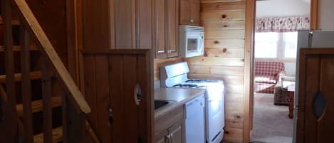 A wooden cabin interior with a kitchen area, including a stove, microwave, and cabinets.
