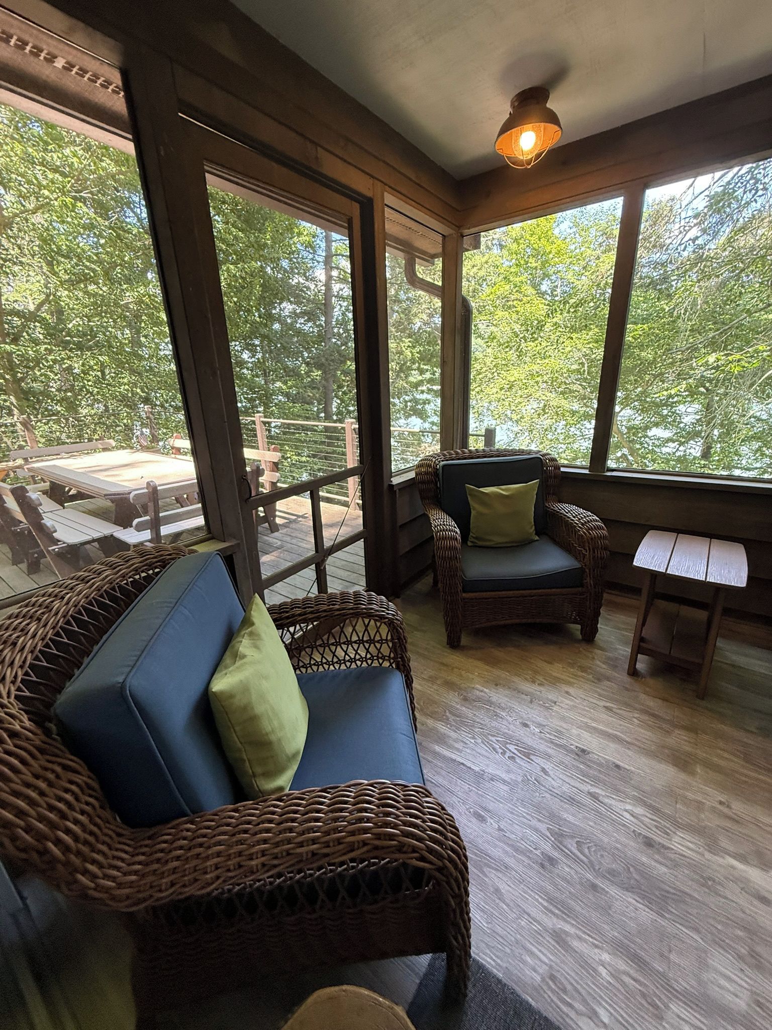 Ein Wintergarten mit Korbmöbeln, großen Fenstern und einer Deckenleuchte.