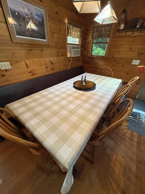 A wooden interior with a checkered tablecloth, wooden chairs, a wall-mounted air conditioning unit, and a framed picture. - Michael's Big Woods Lakefront Chalet with WIFI, AC and water toys (Greentown)