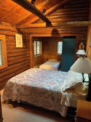 A log cabin bedroom with a bed, a nightstand, a lamp, and a framed picture on the wall.