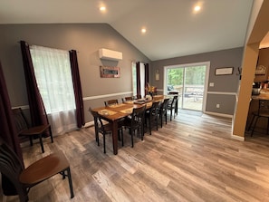 A dining area with a long table and chairs, a window with curtains, and a view of the outdoors.