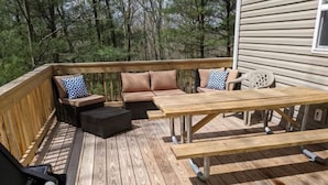 Een houten terras met tuinmeubilair, waaronder een bank, stoelen en een tafel.
