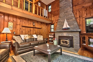 A cozy living room with a fireplace, wooden walls, a leather sofa, and a coffee table. - Sunny Point Lake Wallenpaupack Lakefront with private dock - 4 bedroom sleeps 9 (Lakeville)
