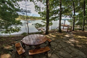 Mesa de piquenique com bancos, um deck de madeira e vista para um lago.