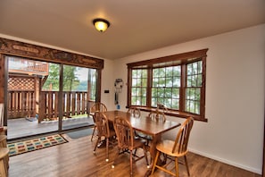 A dining area with a wooden table and chairs, large windows with a view of trees, and a ceiling light fixture. - Twin Cottages on Lake Wallenpaupack – Your Glamping Getaway - Sleeping 14 - 20 (Greentown)