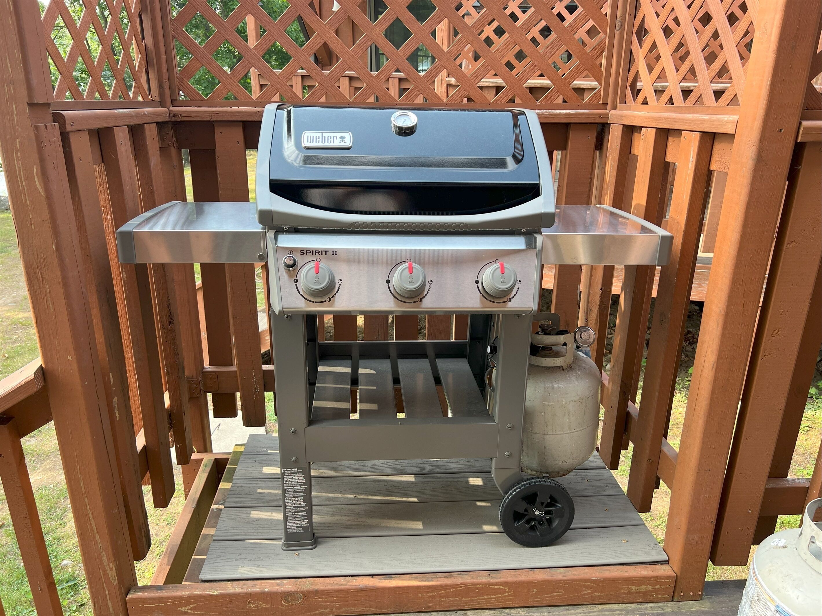 Una parrilla portátil Weber Spirit II con tres quemadores y repisa lateral, sobre una terraza de madera.