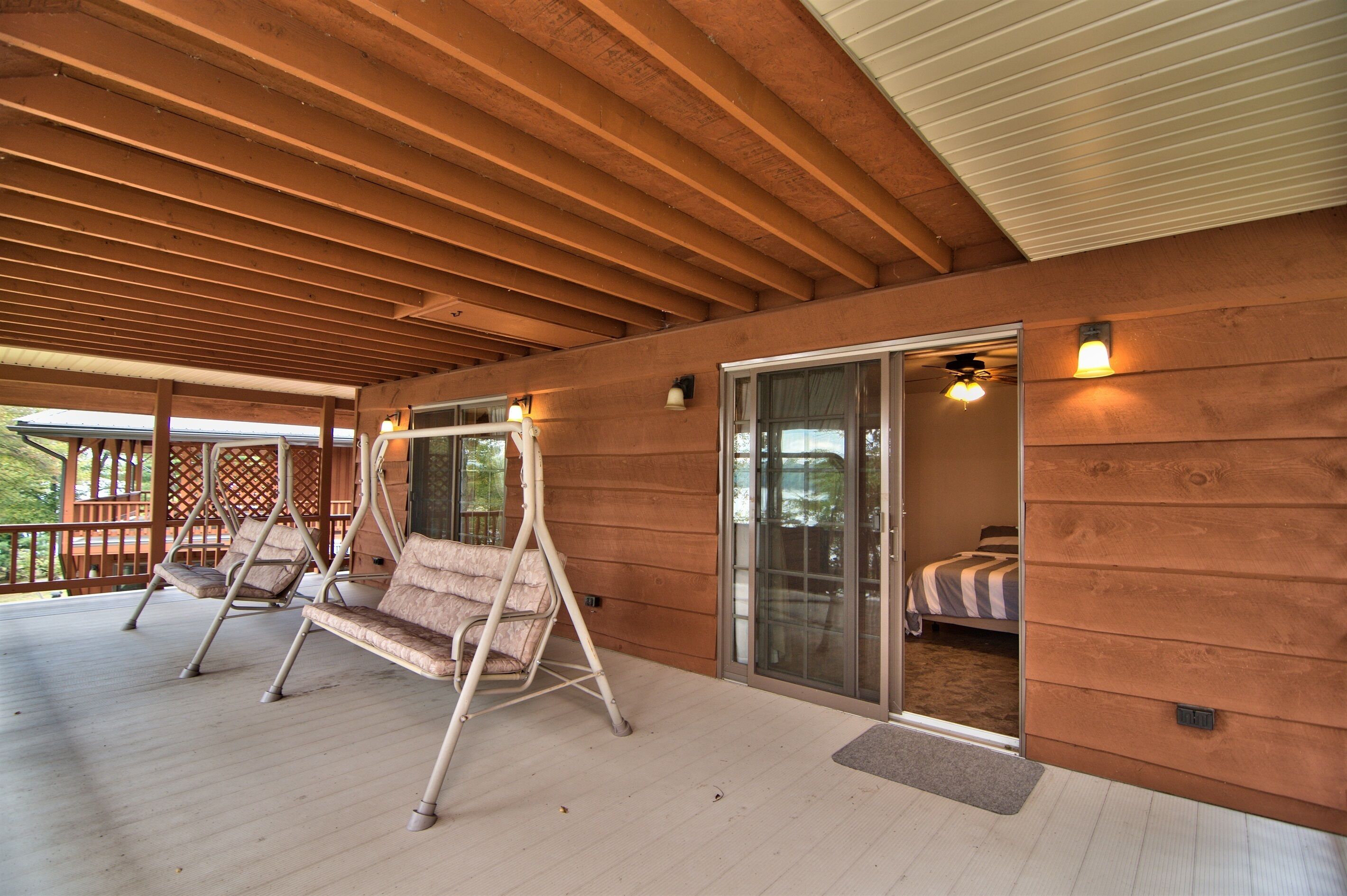 Una terraza de madera con dos asientos tipo columpio y un ventanal corredera que da a un dormitorio.