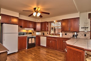A kitchen with wooden cabinets, a refrigerator, a microwave, a stove, a dishwasher, and a ceiling fan. - Twin Cottages on Lake Wallenpaupack – Your Glamping Getaway - Sleeping 14 - 20 (Greentown)