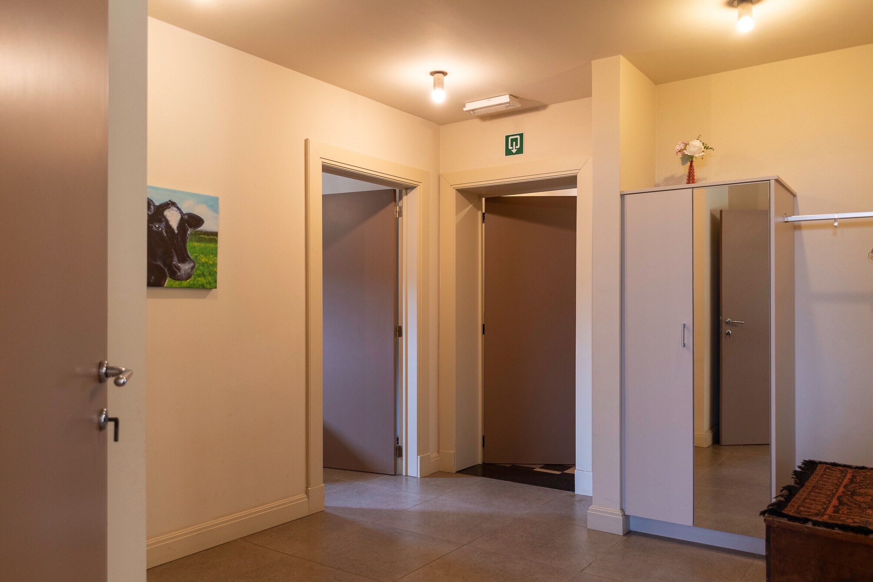 Corredor de hotel com uma porta à esquerda, um espelho à direita e um sinal de saída verde acima.