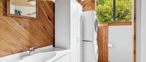 A compact, modern bathroom with a wooden interior, a white sink, and a built-in washing machine.