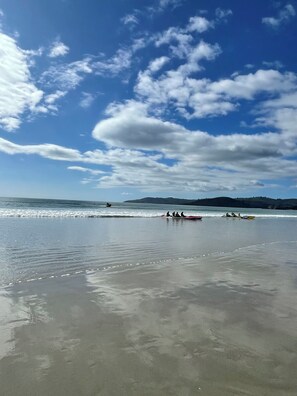 Uma praia com águas calmas, céu claro e colinas ao longe.