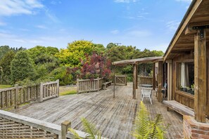 A wooden deck with a pergola, outdoor seating, and a view of a lush garden.