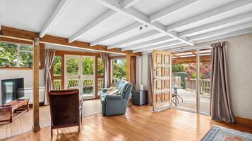 Quarto espaçoso com piso de madeira, sofá, televisão e porta de vidro deslizante para área externa.