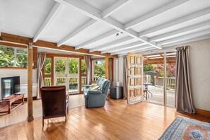 Quarto espaçoso com piso de madeira, sofá, televisão e porta de vidro deslizante para área externa.