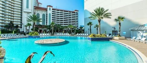 A swimming pool with lounge chairs and palm trees, surrounded by hotel buildings.