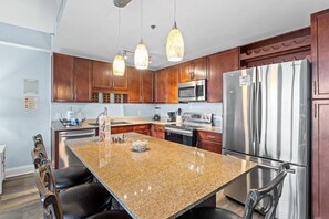 Une cuisine dotée de plans de travail en granit, d’appareils électroménagers en acier inoxydable, d’armoires en bois et de luminaires suspendus.