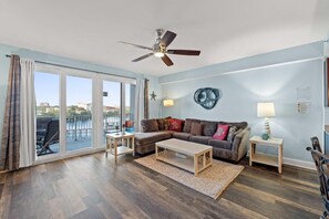 Un salon spacieux doté d’une grande fenêtre, d’un ventilateur de plafond, d’un canapé, d’une table basse et d’une petite table d’appoint.