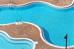 Une grande piscine à bords incurvés, entourée d’une terrasse en briques.