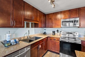 A kitchen with wooden cabinets, stainless steel appliances, a granite countertop, and a dish rack. - Laketown Wharf 316 (Panama City Beach)