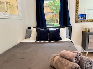A bedroom with a bed, pillows, a window with curtains, a bedside table with a lamp, and a TV on the wall. - Charming 4-Bed Sausalito Home with Bay Views & Garden Patio near San Francisco (Sausalito)