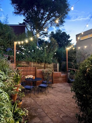 An outdoor patio area with a table and chairs, surrounded by potted plants and a wooden fence. - Charming 4-Bed Sausalito Home with Bay Views & Garden Patio near San Francisco (Sausalito)