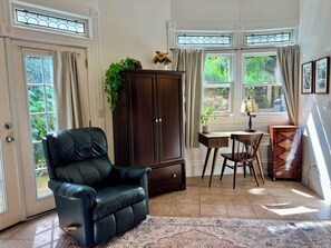 Una habitación con una silla de cuero, un escritorio de madera, un armario y una ventana con cortinas.