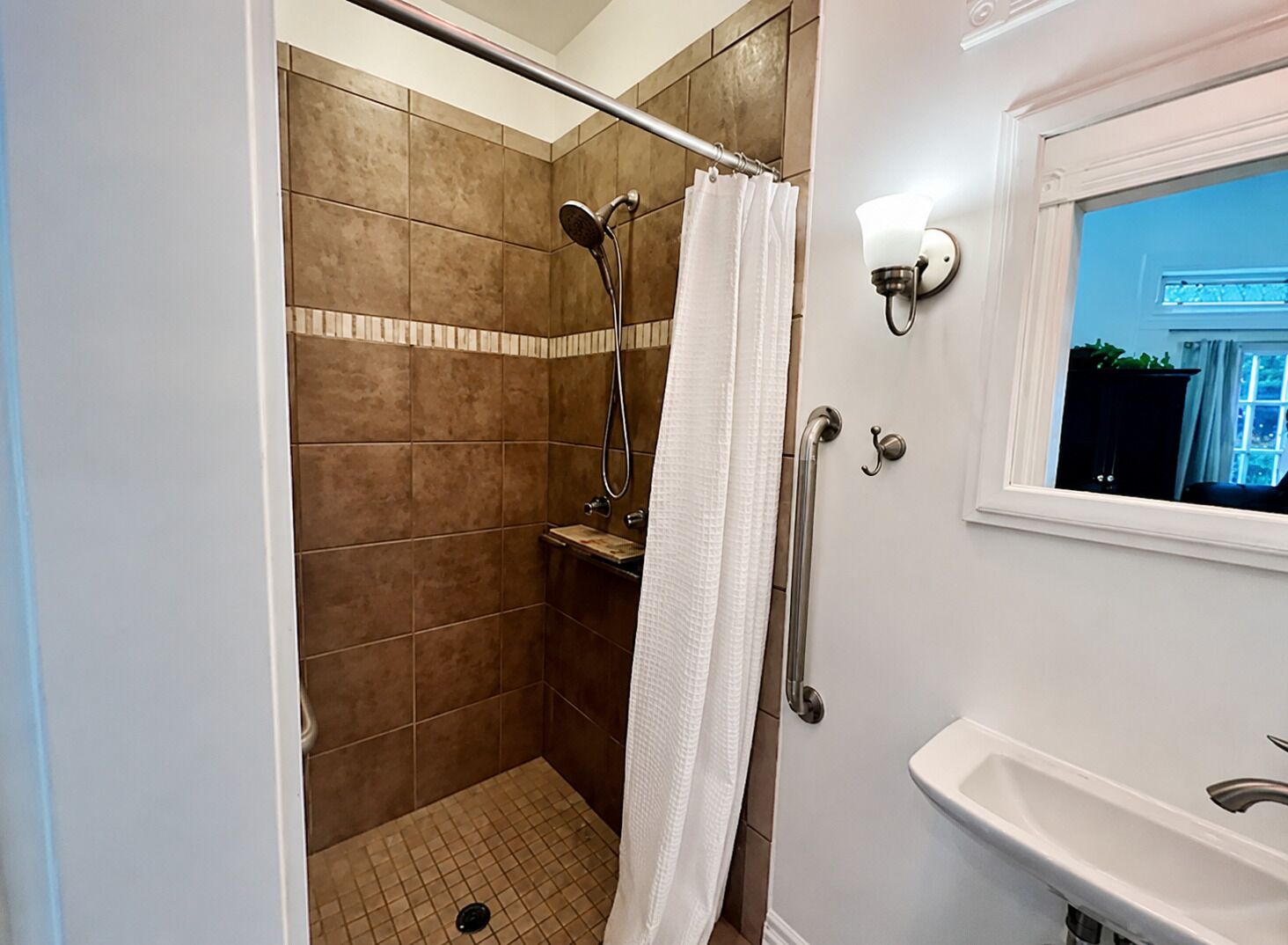 Une salle de bain équipée d’une douche, d’une barre d’appui, d’un lavabo et d’une fenêtre.