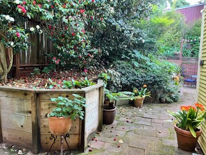 Un jardín con un cantero elevado de madera, plantas en macetas y un sendero de ladrillo.