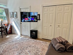 A living room with a flat-screen TV mounted on the wall, a patterned rug, a sofa with rolled-up towels, a small black speaker, and a door with a window. - Charming 4-Bed Sausalito Home with Bay Views & Garden Patio near San Francisco (Sausalito)