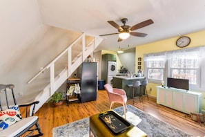 A compact living space with a kitchen, dining area, and a staircase leading to an upper level. - All Points’ End (HOUSE) (Naples)