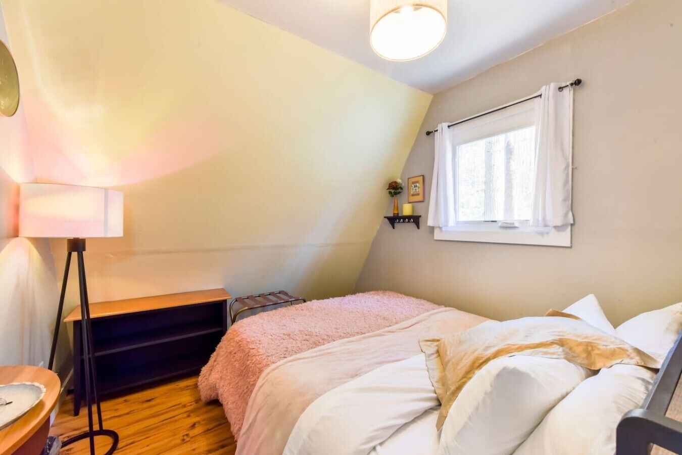 Une chambre à coucher comprenant un lit, une table de chevet, une lampe, une fenêtre avec des rideaux et une étagère ornée d’objets décoratifs.