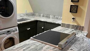 A compact kitchen with a built-in washer and dryer, a countertop with a coffee cup, and a wall-mounted outlet.