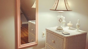 A room with a large mirror, a bedside table with a lamp, and a dresser.