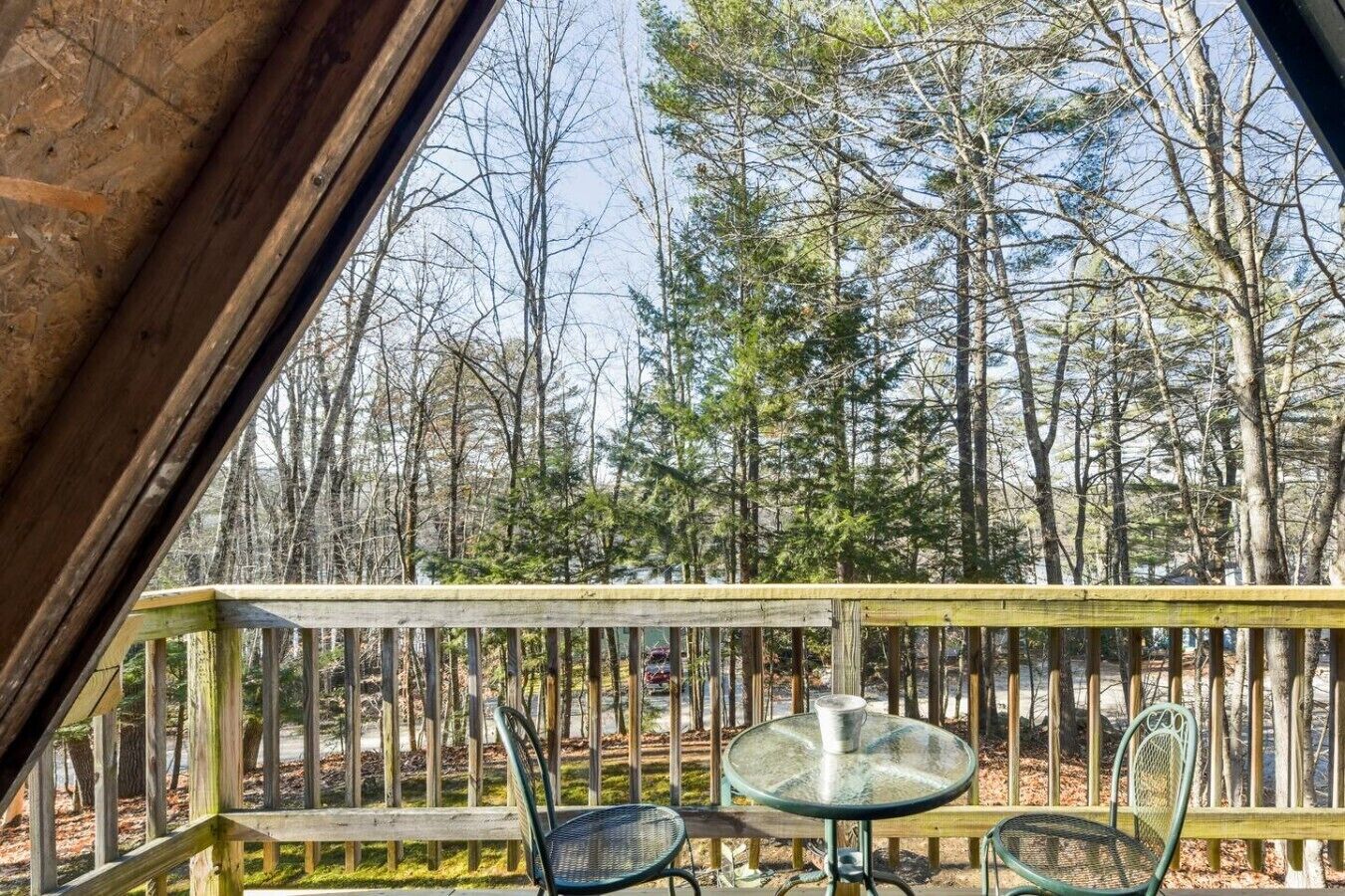 Une terrasse en bois avec une table en verre et deux chaises, donnant sur une zone boisée.