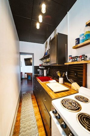 Een moderne keuken met een houten aanrecht, een rode spoelbak en een fornuis. Er zijn keukenkastjes en een afzuigkap boven het fornuis.