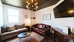 Una sala de estar con un sofá, un sillón de cuero rojo, una mesa de centro, un tapete, un televisor y una chimenea.