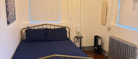 Ein Schlafzimmer mit einem Bett, einem Heizkörper, einem kleinen Tisch mit Lampe und einer Wand-Klimaanlage.