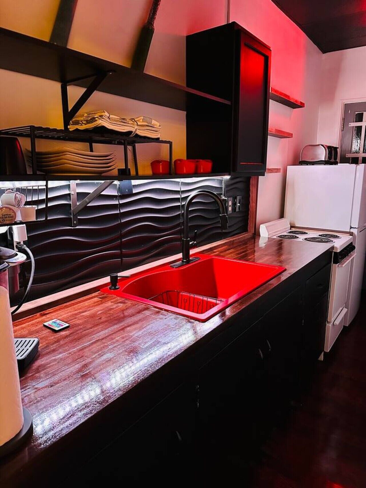 Une cuisine moderne avec un évier rouge, des armoires noires et un revêtement mural original.