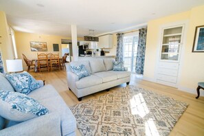 A living room with a sofa, a dining table with chairs, a kitchen area, and a patterned rug.