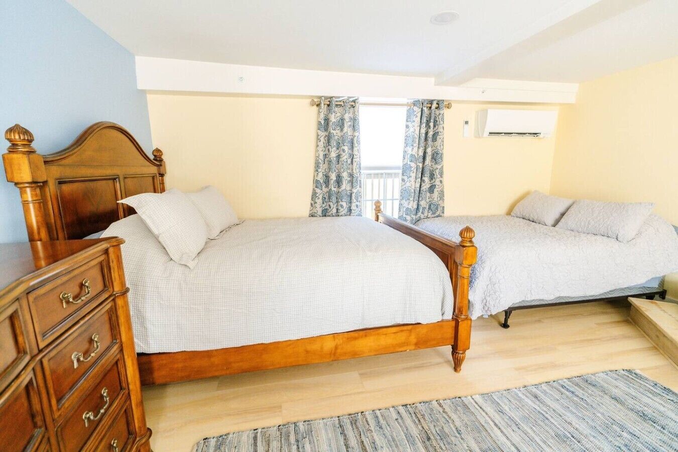 Une chambre à coucher avec deux lits en bois, une commode en bois, une fenêtre avec des rideaux et un ventilateur de plafond.