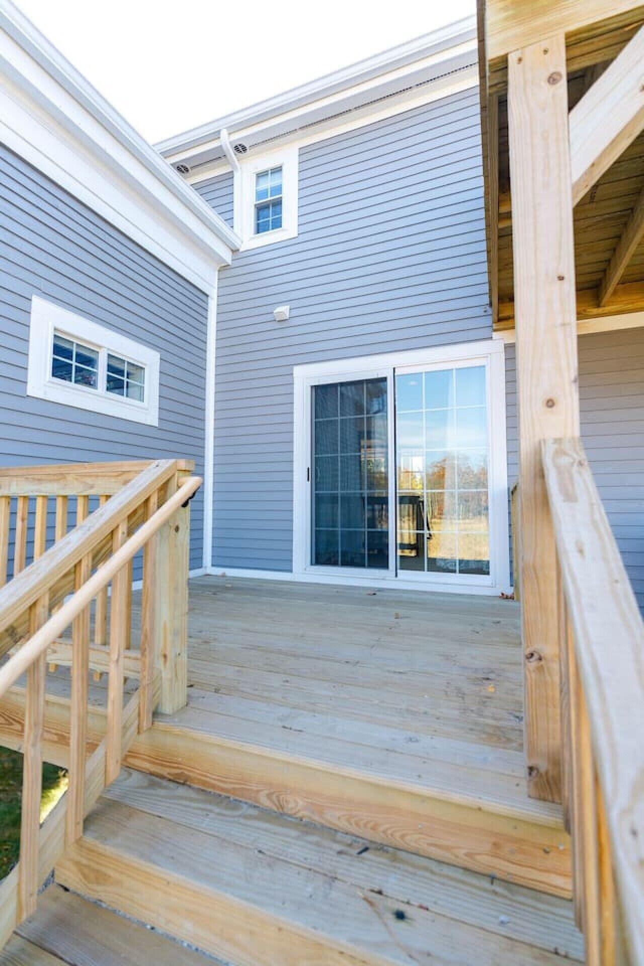 A wooden deck leading to a house with a grey exterior and a sliding glass door.