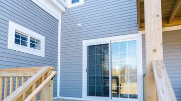 A wooden deck leading to a house with a grey exterior and a sliding glass door.