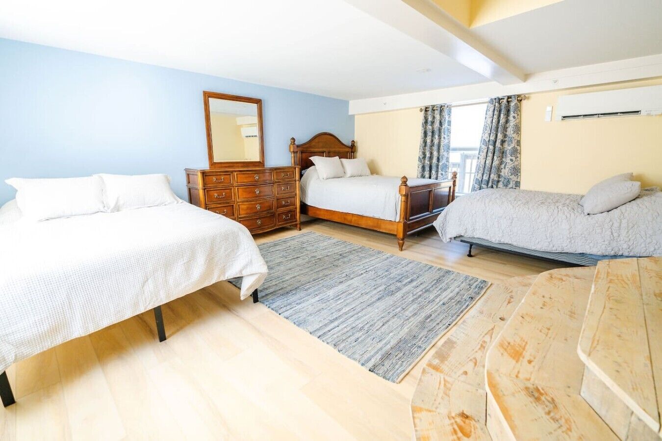 A bedroom with two beds, a dresser, a mirror, and a window with curtains.