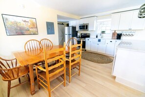 Een keuken met witte kastjes, een houten eettafel met stoelen en een koelkast.