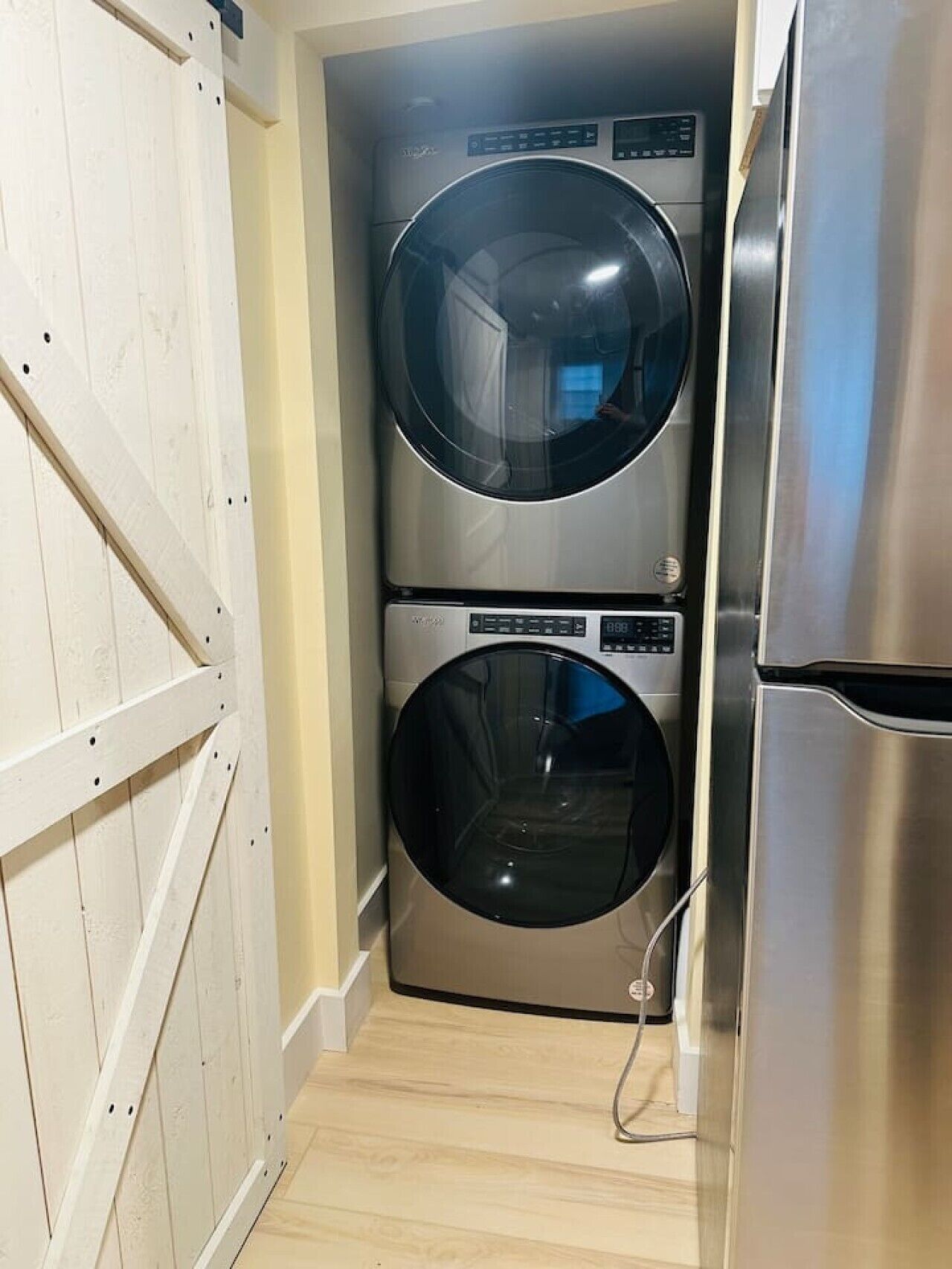A compact laundry room with a stainless steel washer and dryer, a wooden door, and a light-colored floor.