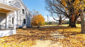 A residential property with a covered porch, a pathway, and a large tree with autumn leaves.