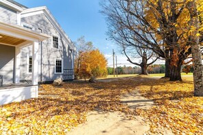 A residential property with a covered porch, a pathway, and a large tree with autumn leaves.
