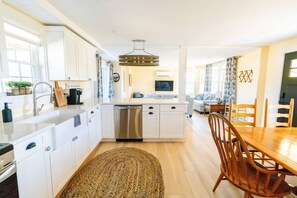A modern kitchen with white cabinetry, a stainless steel dishwasher, and a dining area with a wooden table and chairs.
