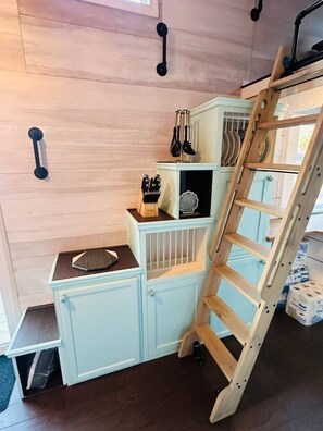 A corner of a room with a light blue cabinet, a wooden ladder, and a set of black wall hooks.