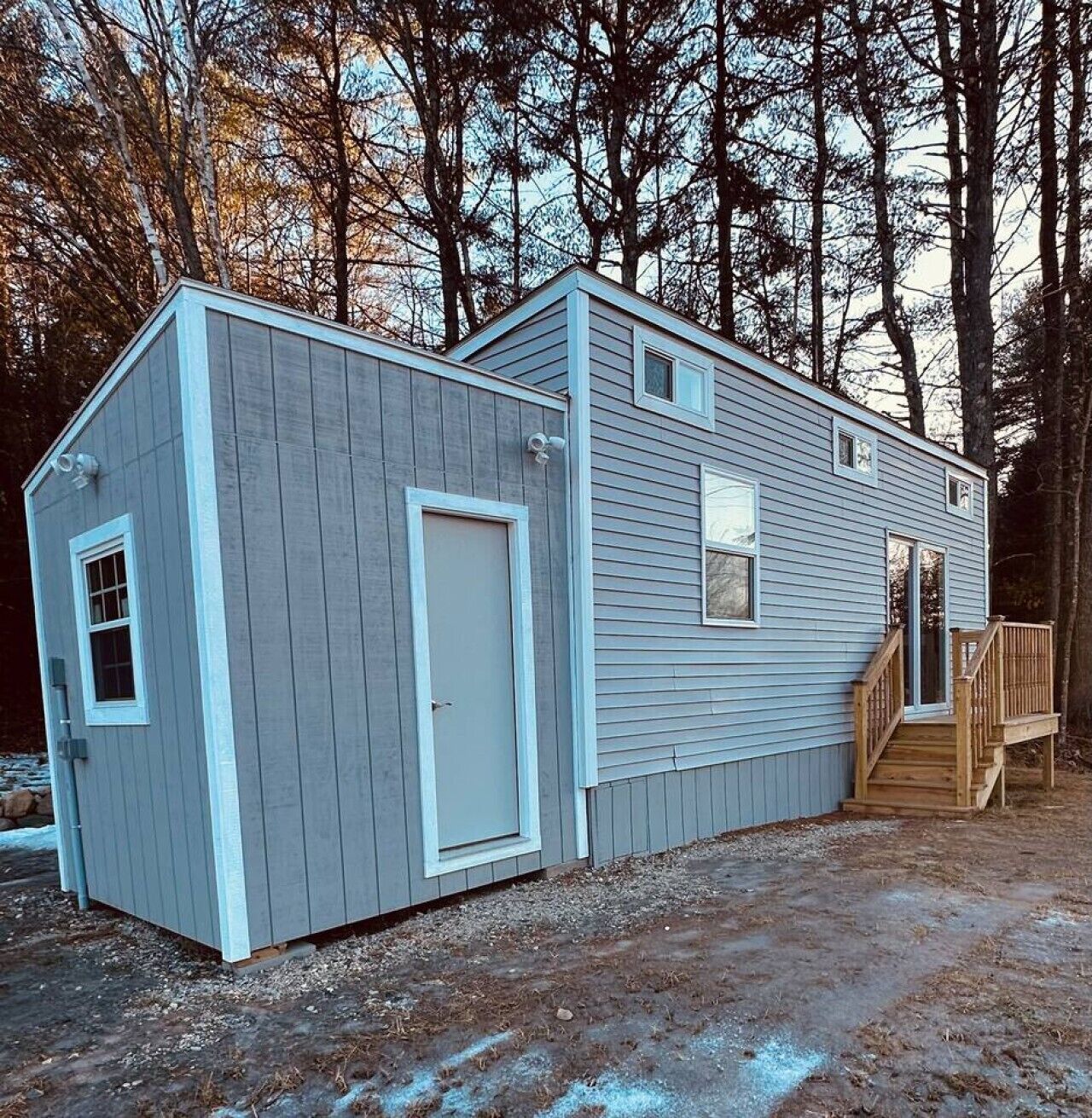 A two-story shed with a door and windows, a wooden deck, and a staircase leading to a porch.